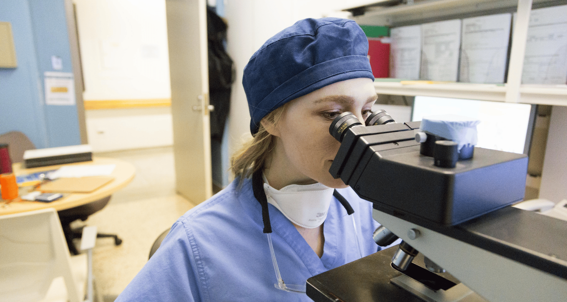 doctor in scrubs looking through a microscope